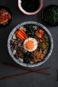 assorted bibimbap vegetables and rice topped with egg in stone bowl on dark gray surface
