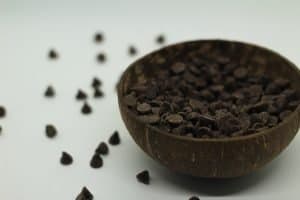 chocolate chips in a brown bowl on a white surface with chocolate chips scattered outside of bowl