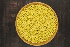 yellow turmeric dried couscous in light brown wooden bowl on dark brown wooden surface