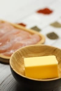 Stick butter in a light brown wooden bowl and chicken and spices in background