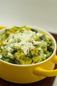 Lemon cucumber herb couscous salad topped with feta in a yellow bowl.
