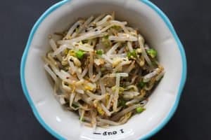 Bibimbap - Seasoned mung bean sprouts in a white bowl with a light blue rim on grey surface