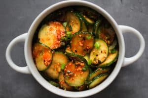 Bibimbap - Gochujang marinated cucumber salad in a white bowl with handles on a grey surface