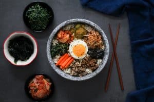 bowl of bibimbap with assorted vegetables in a Korean stone bowl dolsot and brown chopsticks on grey surface