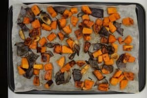 Roasted butternut squash, onions, and garlic on a parchment lined baking sheet.