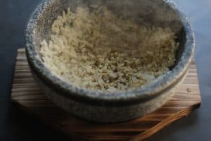 Bibimbap - black and white speckled korean stone bowl on brown wooden base with layer of steaming rice spread evenly around bowl
