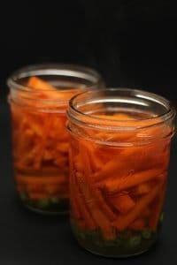 Bibimbap - two ball mason jars filled with sliced scallions, minced garlic, sliced carrots and pickling liquid on black surface