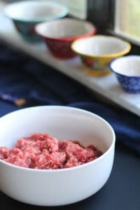 Bibimbap - marinated raw ground beef in a white bowl with colorful dishes on windowsill blurred in the background