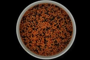 Bibimbap - orangeish red bibimbap sauce with lots of tri-colored sesame seeds in a white bowl on black surface