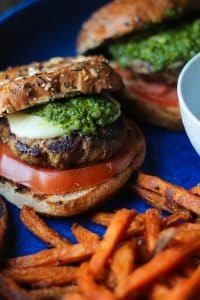 caprese turkey burgers with tomato mozzarella and basil vinaigrette on dave's killer bread buns on a blue stone platter with sweet potato fries