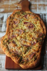 cheesy flatbread pizza with salami and honey goat cheese almond pesto on a brown cutting board on brown and white wooden surface