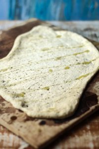 prepared flatbread pizza dough drizzled with oil and sprinkled with salt and pepper on pizza stone