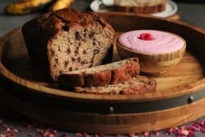 loaf of chocolate chip banana bread with two slices and a bowl of raspberry mascarpone cream
