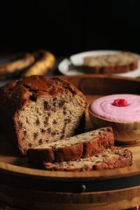 loaf of chocolate chip banana bread with two slices and a bowl of raspberry mascarpone cream