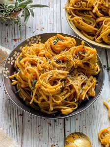 Pasta with Roasted Garlic Butternut Squash Sauce in a gray bowl on a white wooden surface