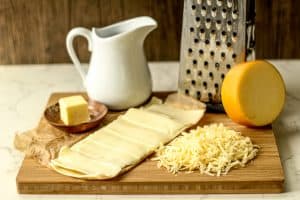 american cheese, smoked gouda cheese, dish with butter, milk, and cheese grater on a cutting board