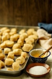 raw soft pretzel bite dough on a silver sheet pan with a bowl of melted butter and a dish of coarse kosher salt on the side, before brushing