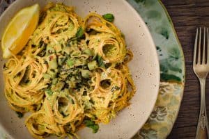 Asparagus Pesto Pasta with Minty Sugar Snap Peas in a matte speckled stone bowl on a brown wooden surface with a fork on the side