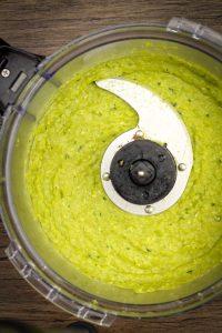 overhead shot of smooth and creamy asparagus pesto in a large food processor on a brown wooden surface