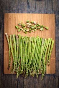 Asparagus on a wooden cutting board with the woody ends cut and displayed