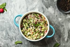 bowl of cucumber and radish salad with mint in a round bowl with blue handles on a gray and white granite surface