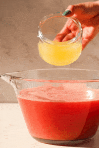 Lemon juice being added and poured into a big glass bowl of watermelon and ginger juice