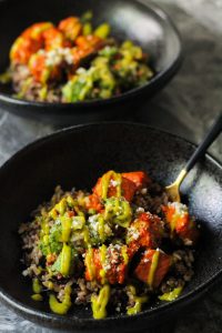 Salmon Rice Bowls with Avocado Salsa and Mango Sauce in a black bowl with a black and gold fork