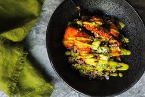Salmon Rice Bowls with Avocado Salsa and Mango Sauce in a black bowl with a fringed green napkin