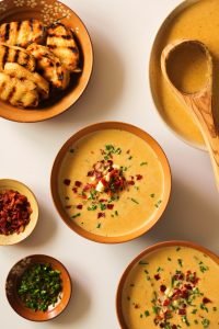 instant pot potato corn chowder with bacon in a tan bowl with chives and bacon in tiny bowls on the side and a bowl with toasted baguette