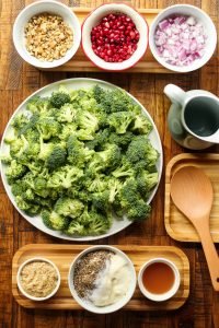 Broccoli pomegranate salad ingredients in separate bowls on a wooden surface.