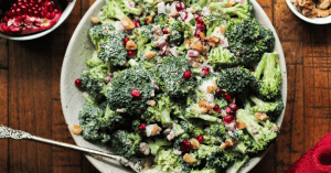 Broccoli pomegranate salad recipe in a white bowl with a halved pomegranate on the side.