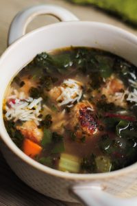 close up of easy Italian wedding soup recipe in a while bowl with rounded handles on a light brown surface