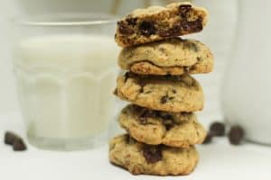 Stack of best easy soft and chewy chocolate chip cookies on a white surface with chocolate chips and a glass of milk in the background.