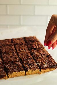 Chocolate maple pecan shortbread bars being sprinkled with flaky salt.