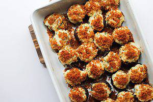 stuffed mushrooms with crab topped with golden brown toasted panko breadcrumbs in a white baking dish on wooden coasters on a white surface.