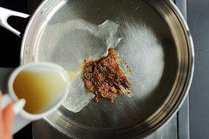 dashi broth being poured into the saucepan with roasted garlic