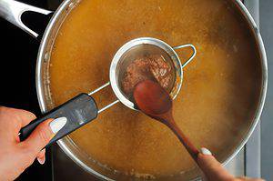 Straining the miso paste into the roasted garlic miso soup recipe using a fine mesh strainer.