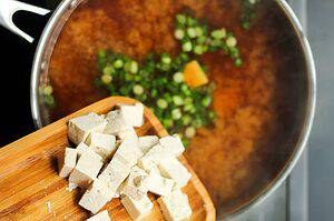 tofu being added to roasted garlic miso soup recipe in a silver pan