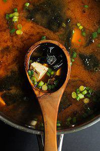 Roasted garlic miso soup recipe in a pan with a wooden spoon holding some.