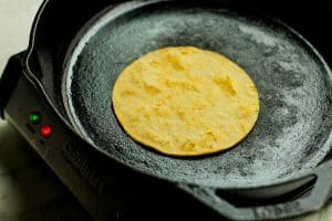 Corn tortilla being warmed in a cast iron skillet.
