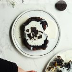 Overhead shot of cookies and cream French toast with cream cheese drizzle and crumbled oreo cookies on a white plate - pinterest pin.