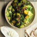 Roasted Brussel Sprout Salad in a tan bowl with a side of blue cheese on a wooden surface - pinterest pin.