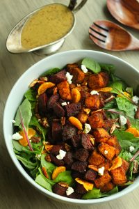 Roasted beetroot and pumpkin salad in a white bowl and mustard vinaigrette and wooden spoons in the background.