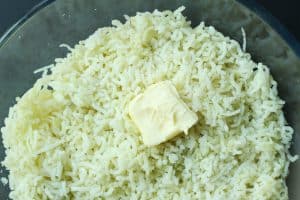 A slab of butter on top of a pile of riced potatoes.