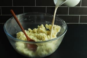 Steeped milk being poured into mashed potatoes with butter.