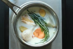 Onion, garlic, and rosemary in milk, in a silver stainless steel pot.