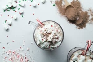 Two clear glass cups of protein hot chocolate. One with whipped cream and one with marshmallows.