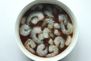 Raw shrimp in a sweet soy marinade in a white bowl.