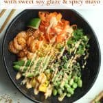 Assembled shrimp poke bowl in a black round bowl with blue and white wooden chop sticks on a white surface.