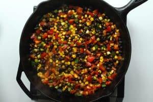 Southwest chicken bowls vegetables (beans, corn, bell pepper, scallions) in a cast iron.